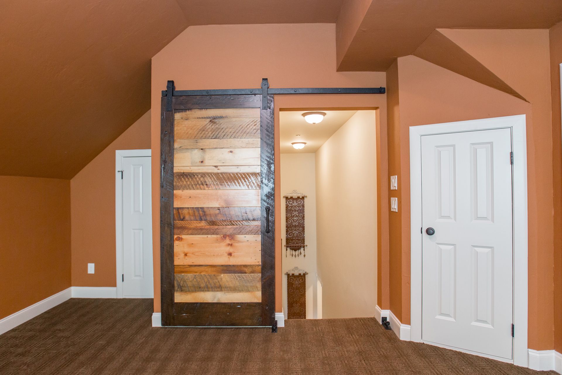 Barn door leading to stairs in a room with orange walls, white doors, and brown carpet.