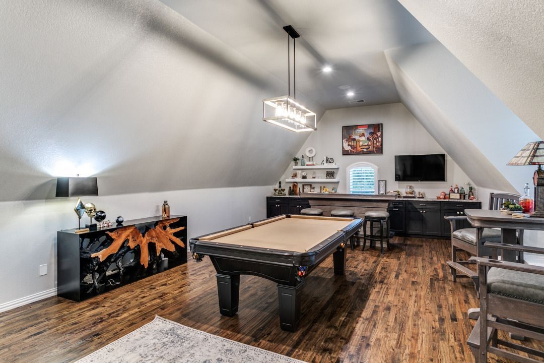 A finished attic game room with a pool table, bar, and seating, with sloped ceilings and wood floors.