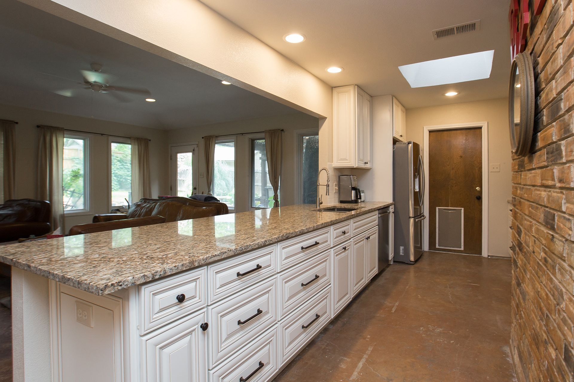 Kitchen with white cabinets, granite countertop, brick wall, and a view into a living room.