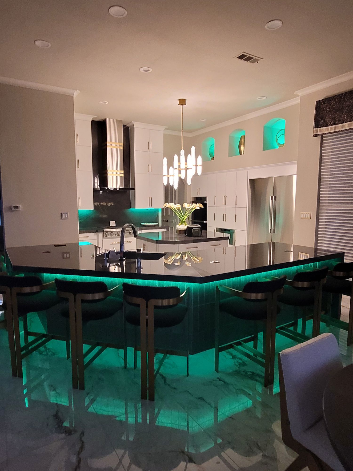 Modern kitchen with an island bar, green lighting, and green velvet bar stools.