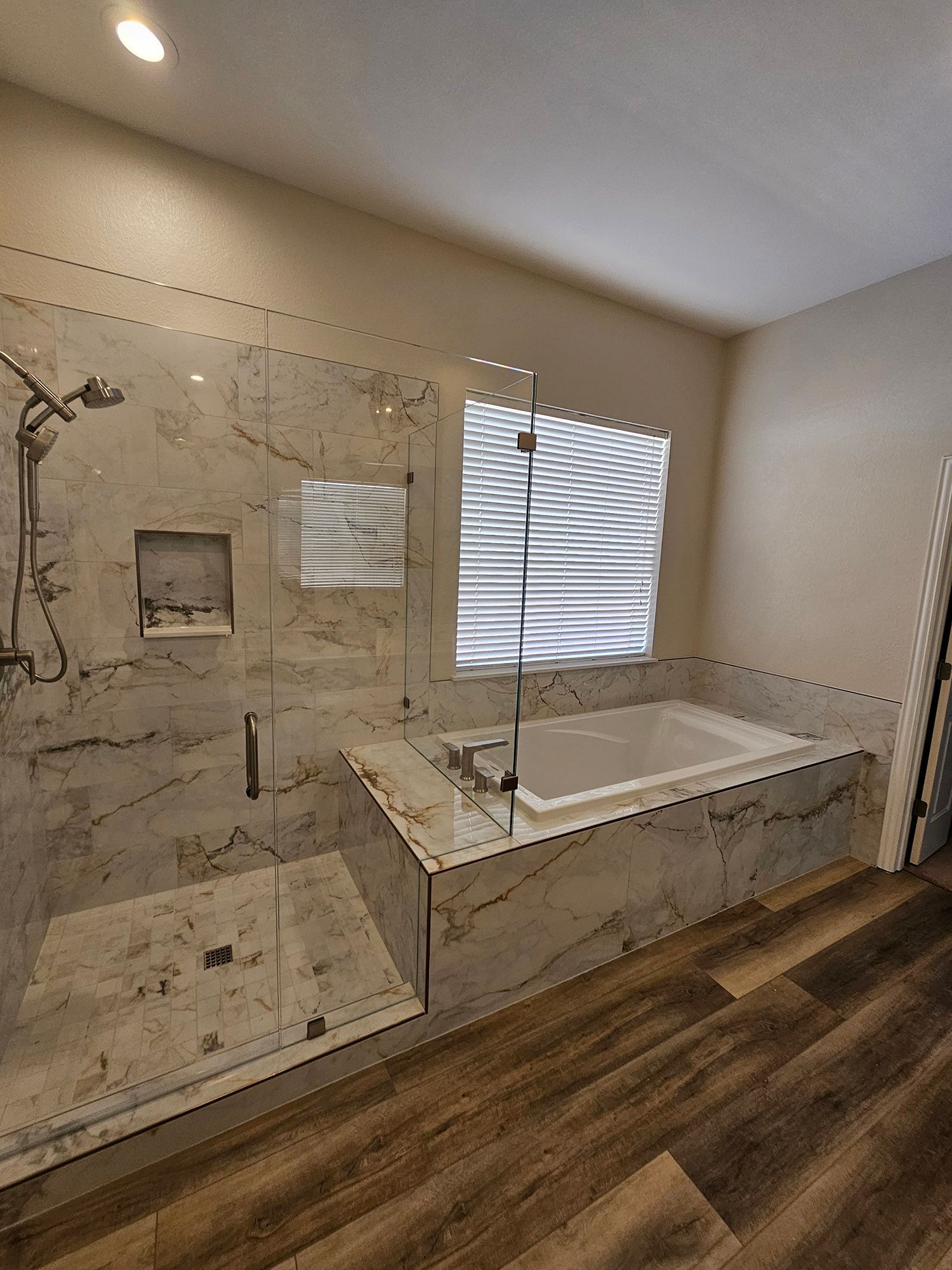 Bathroom with marble-patterned tiles, glass shower, and tub. Wood-look floor.