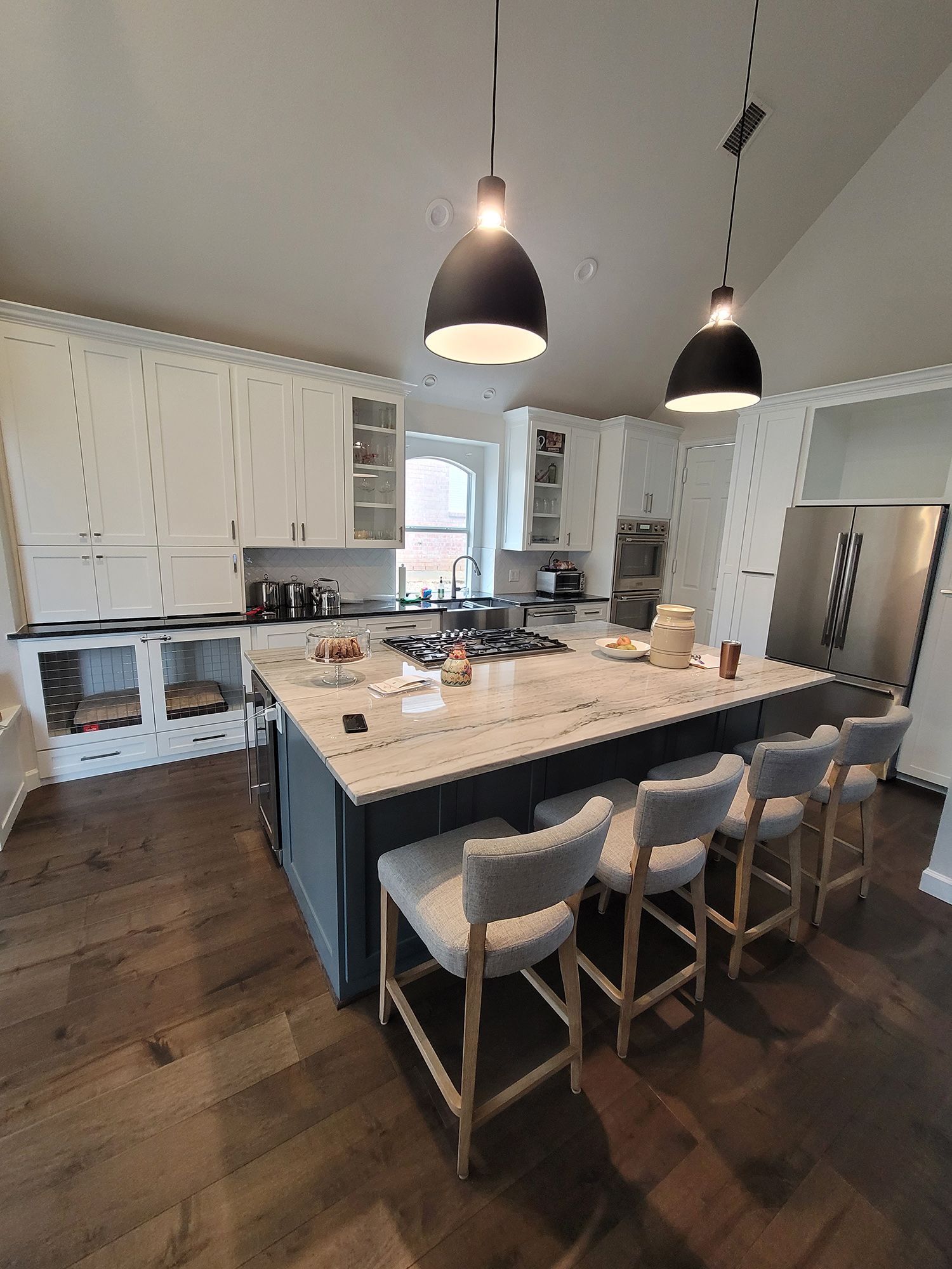 Modern kitchen with white cabinets, a blue island with seating, and dark wood flooring.