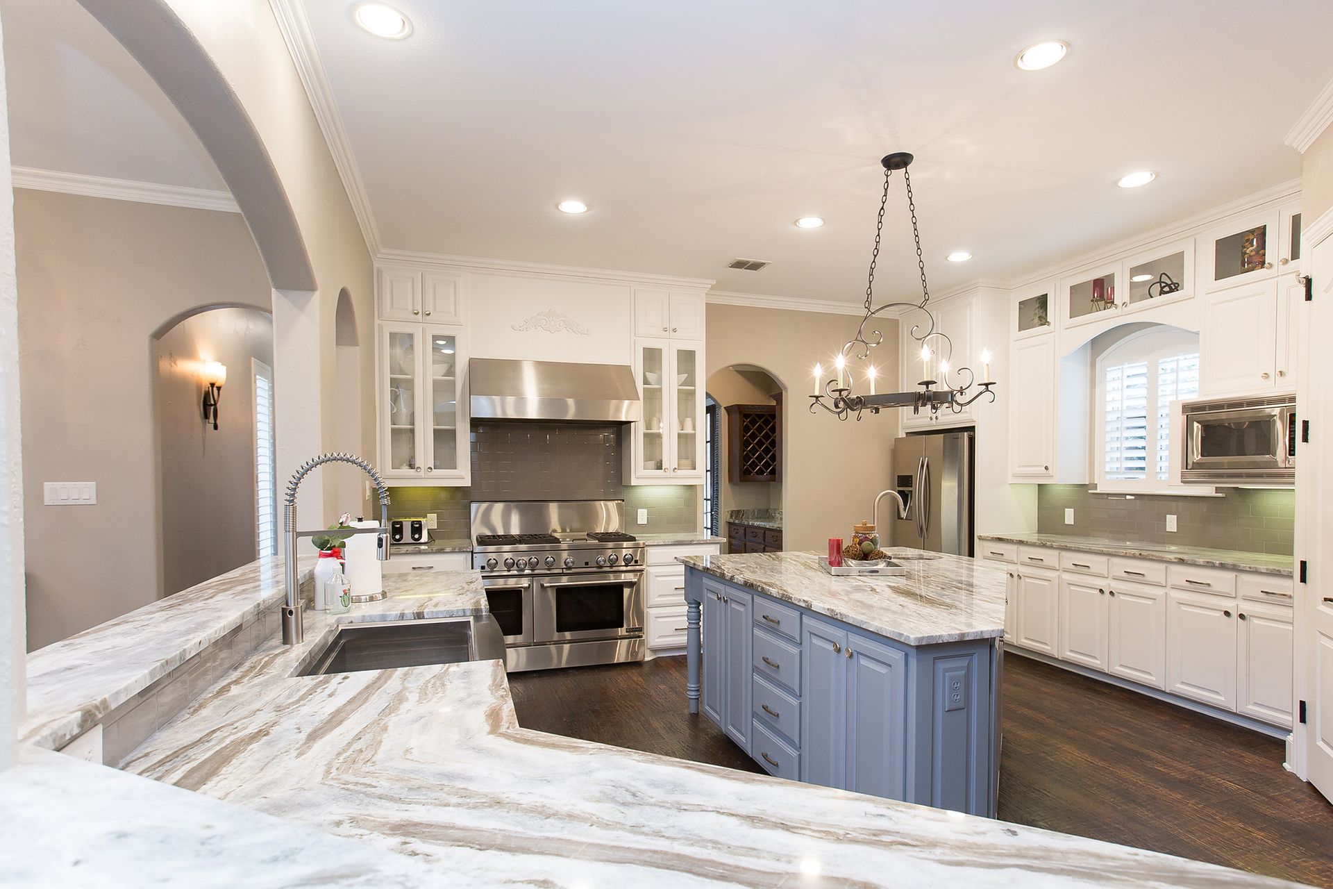 Spacious, elegant kitchen with white cabinets, stainless steel appliances, granite countertops, and a blue island.