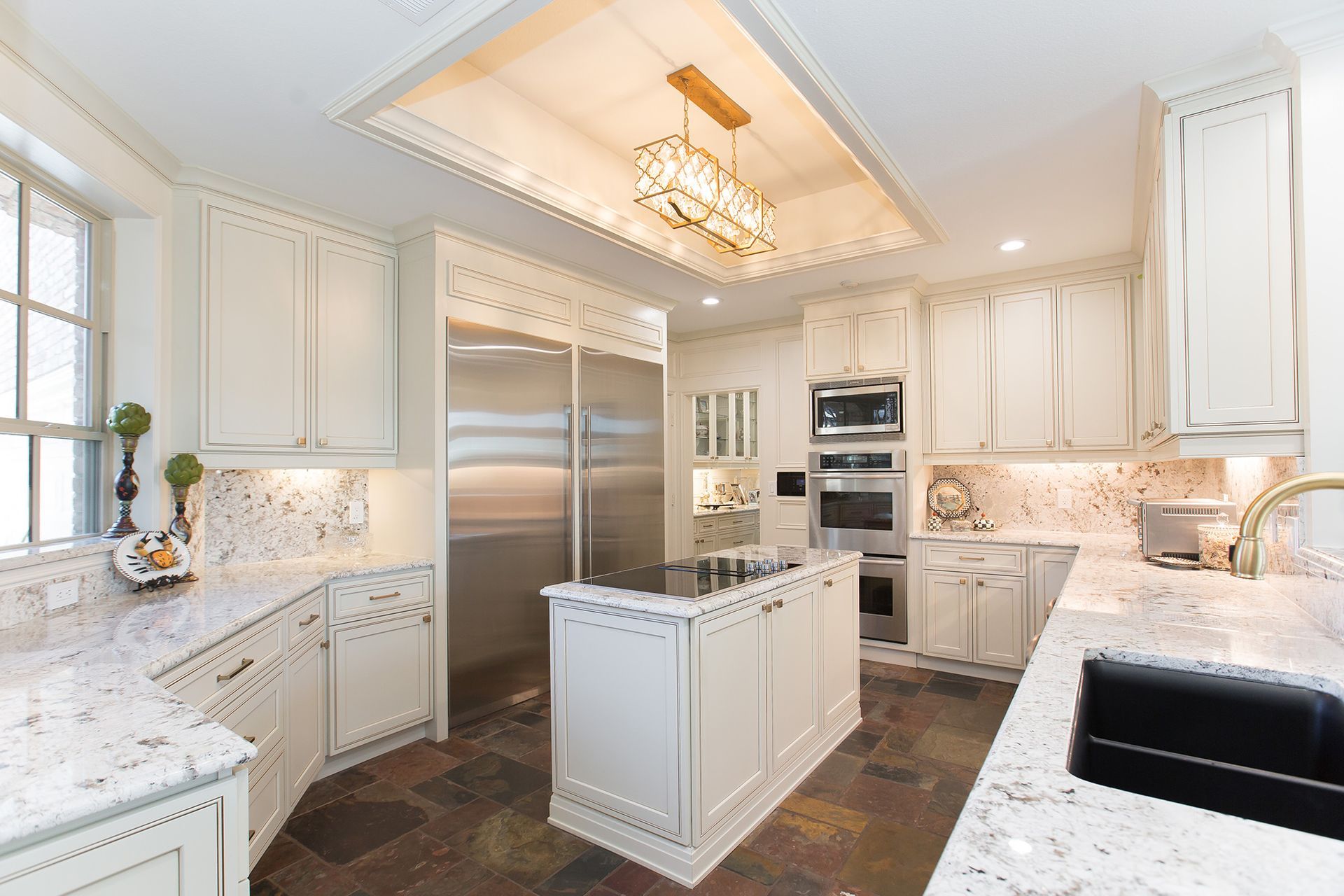 Cream-colored kitchen with granite countertops, stainless steel appliances, island, and stone tile flooring.