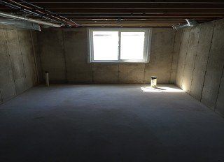 An empty basement with a window and a drain pipe.