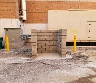 A brick wall is being built in a parking lot next to a building.