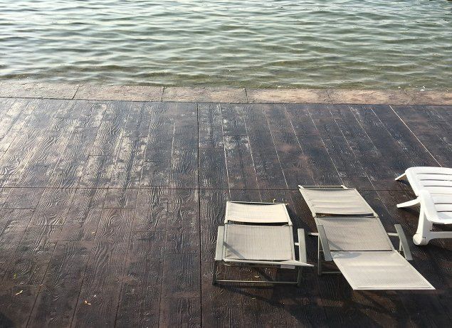 Two lounge chairs are sitting on a wooden deck near the water.