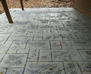 A concrete patio with leaves on it and a brick wall in the background.