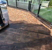 A set of stairs leading up to a deck with a brick wall and glass railing.