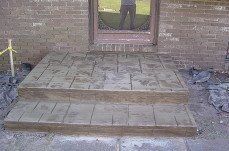 A man is standing on a concrete porch in front of a brick building.