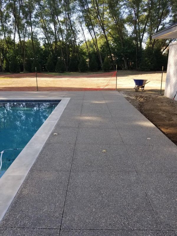 A concrete walkway leading to a swimming pool with trees in the background