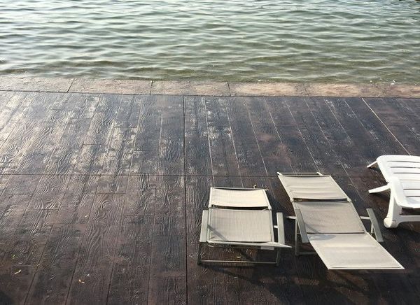 Two lounge chairs sit on a wooden deck near the water