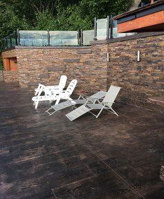 Two white lounge chairs are sitting on a wooden deck next to a brick wall.