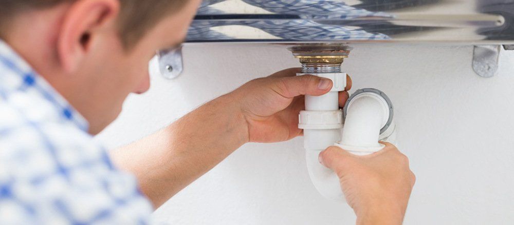 A man is fixing a sink pipe in a bathroom