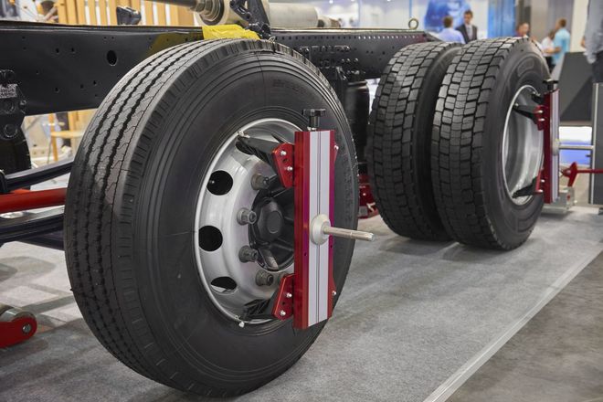Truck chassis with two large rear tires and a red wheel alignment device attached to the front wheel