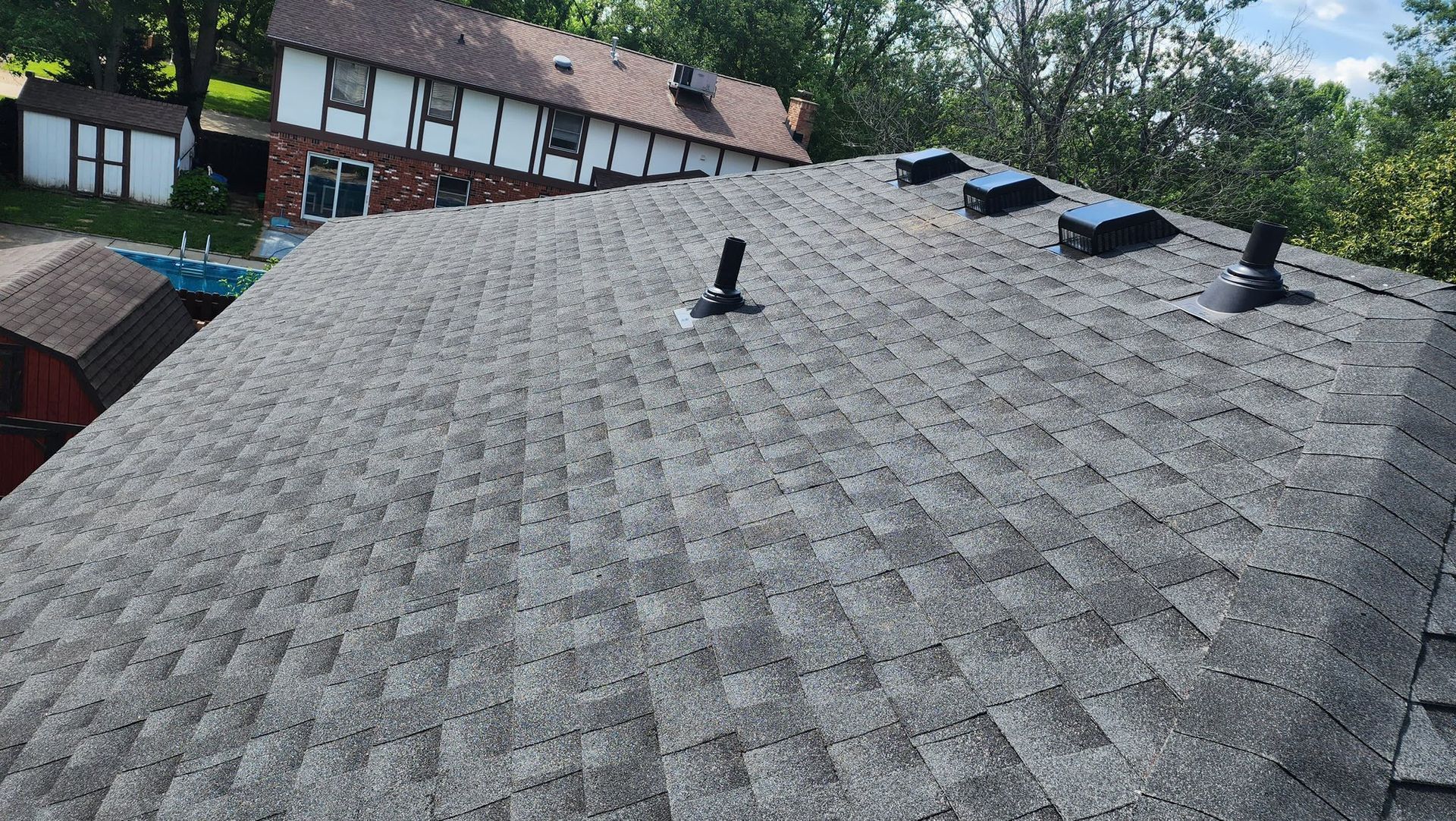 A roof with a lot of shingles on it and a house in the background.