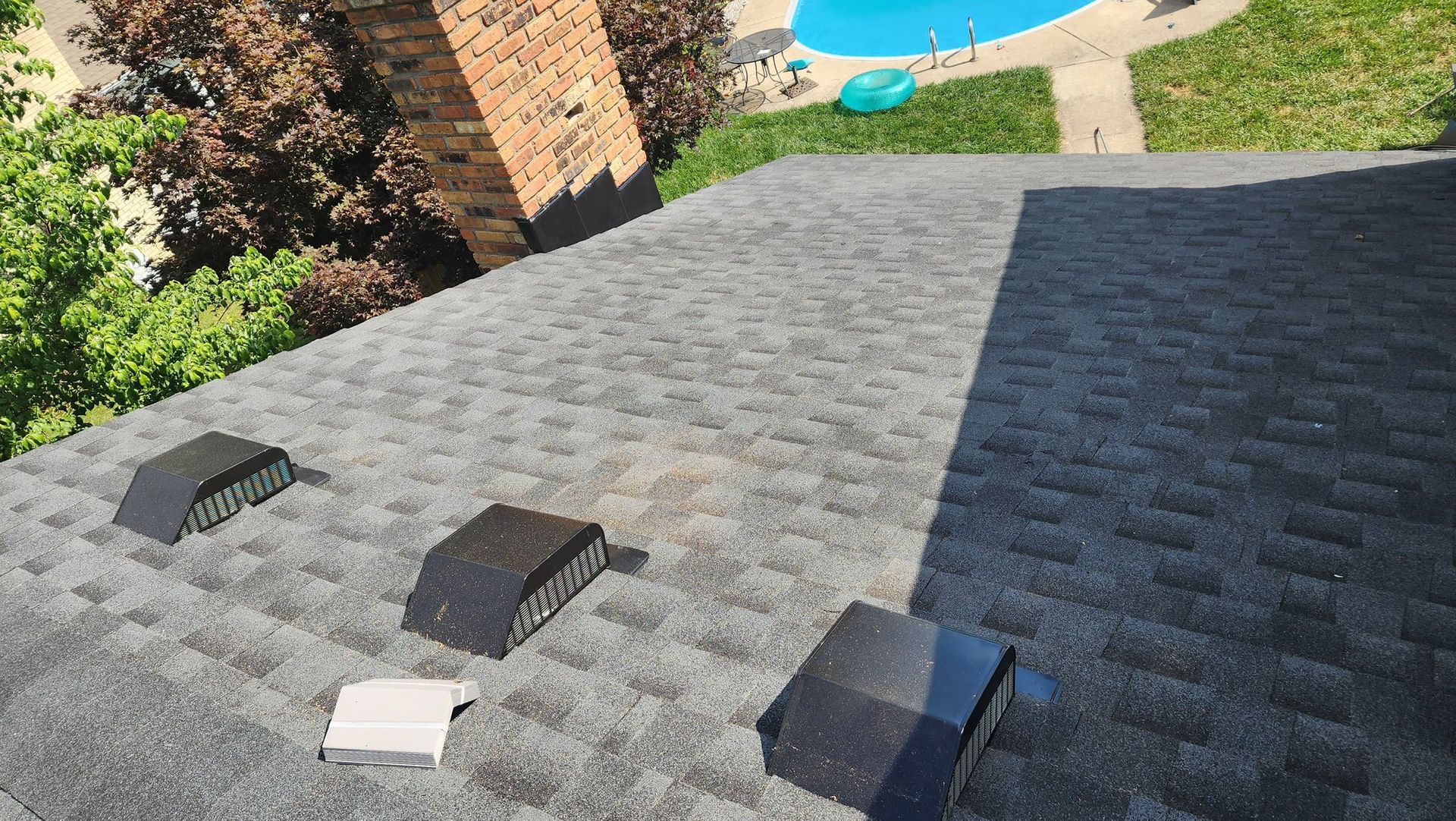 The roof of a house with a swimming pool in the background.