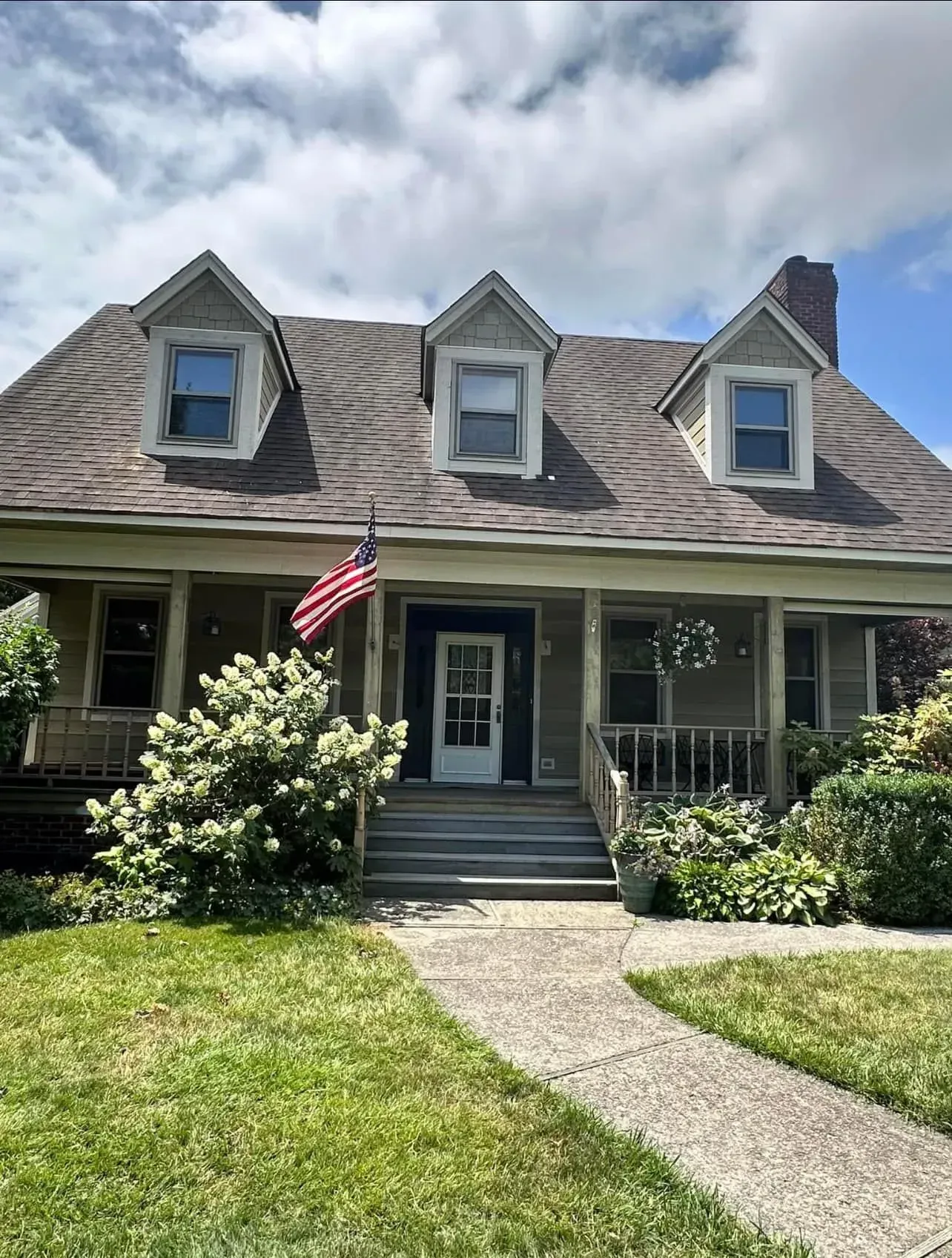 A large house with a porch and an american flag in front of it.