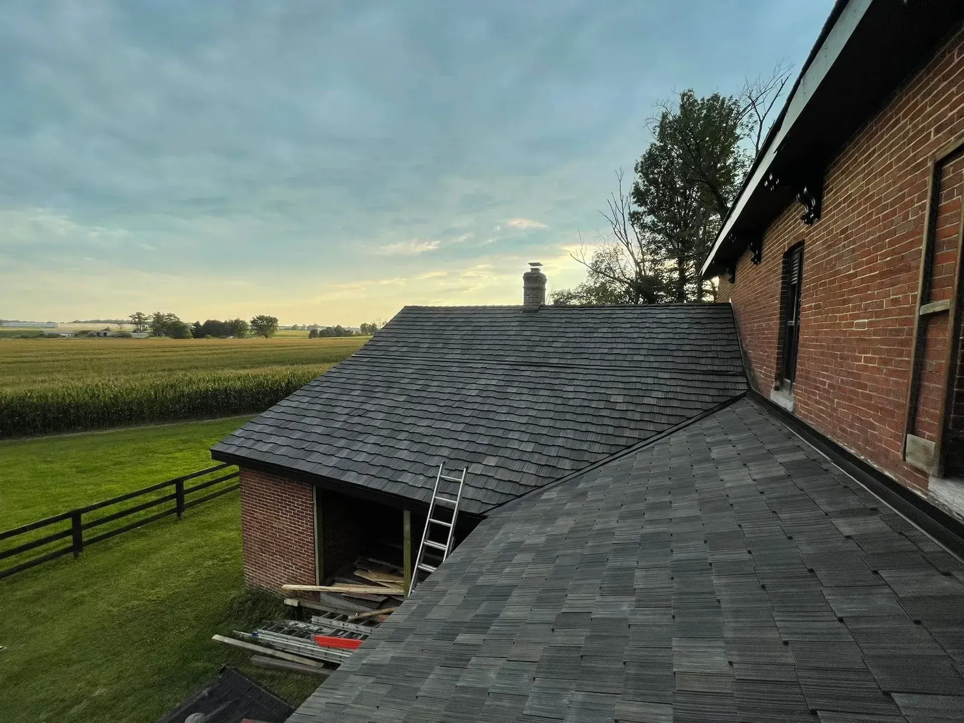 A house with a ladder on the roof and a field in the background.