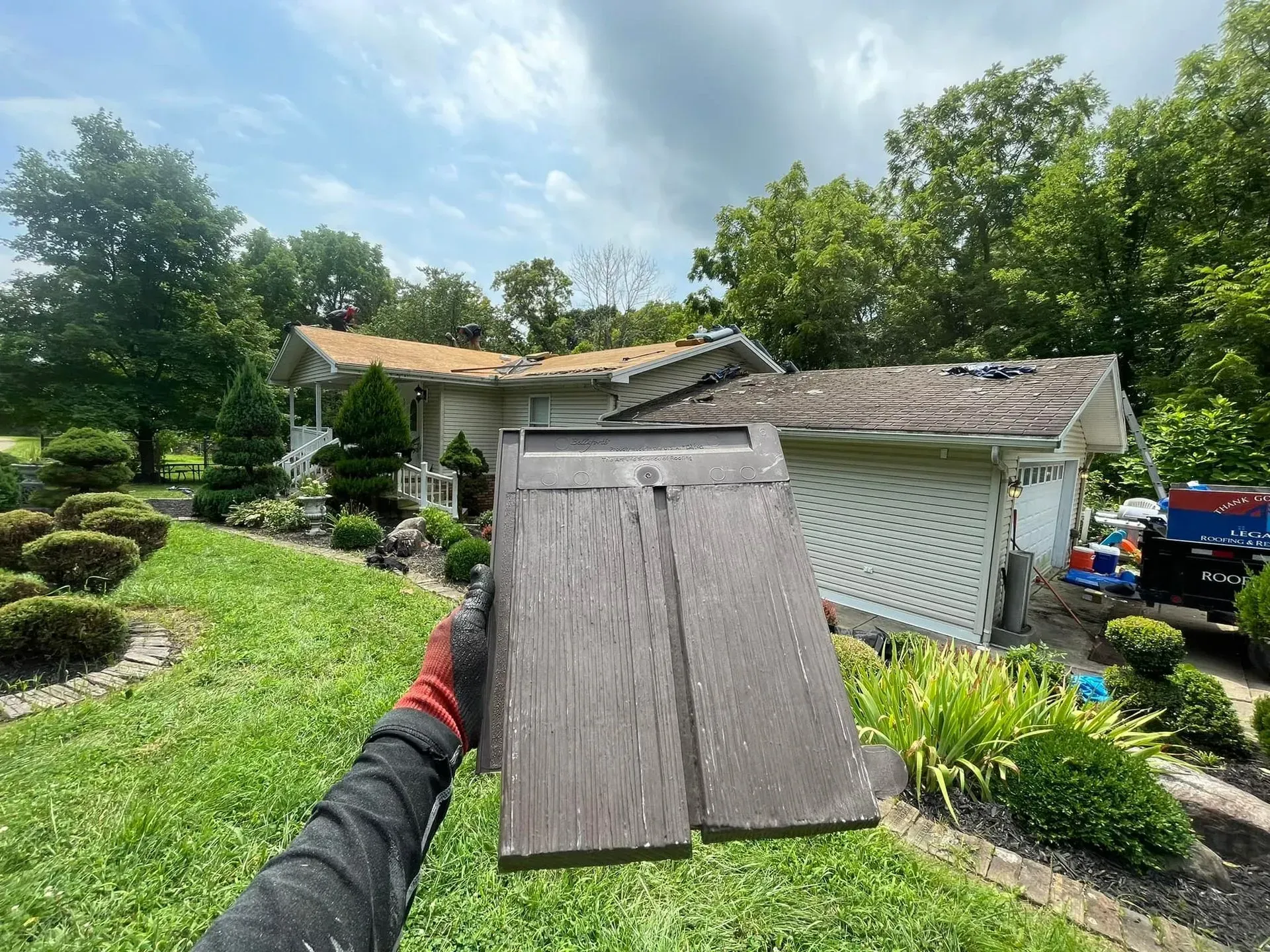 A person is holding a piece of wood in front of a house.
