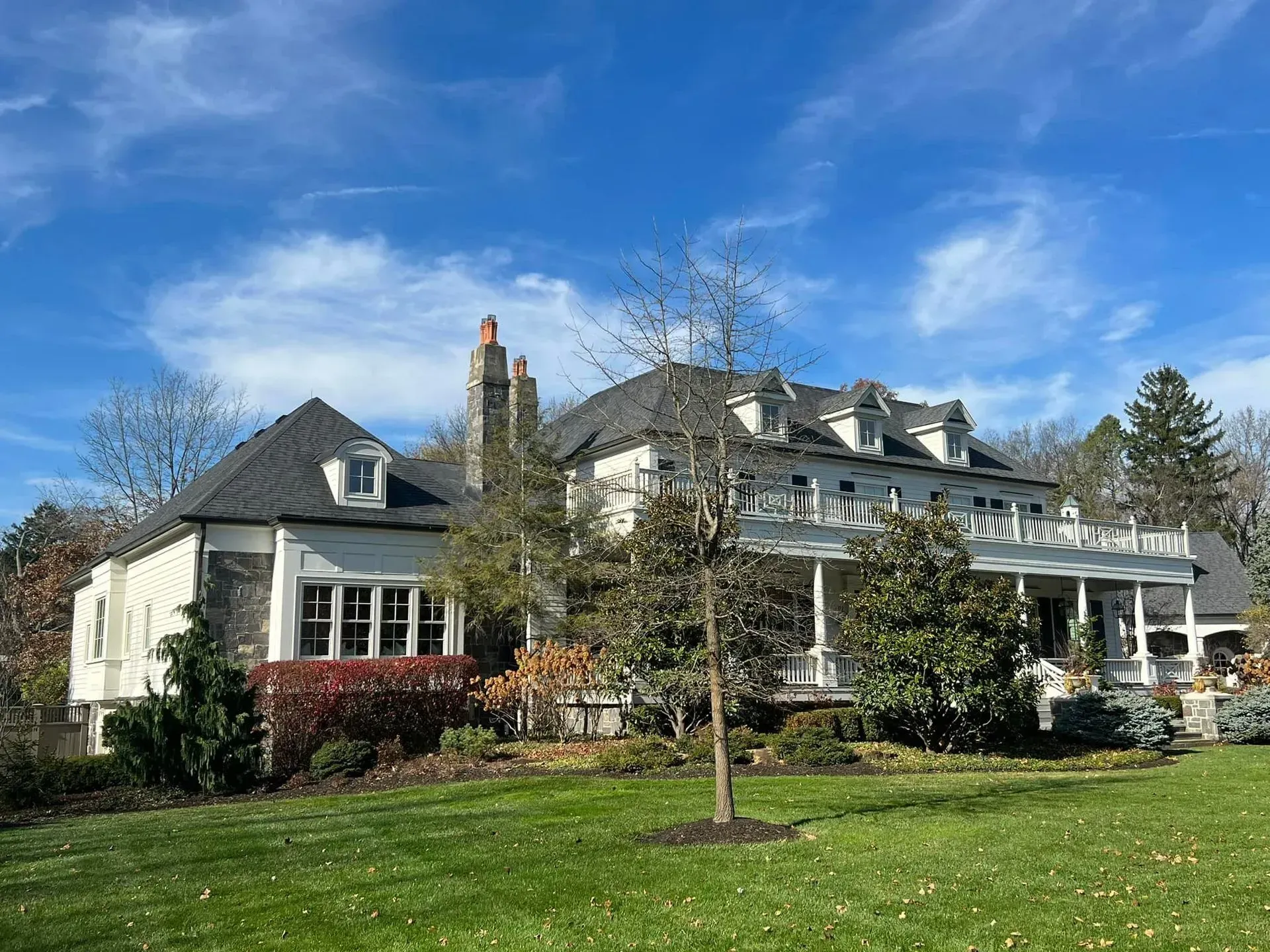A large white house with a large porch is sitting on top of a lush green field.
