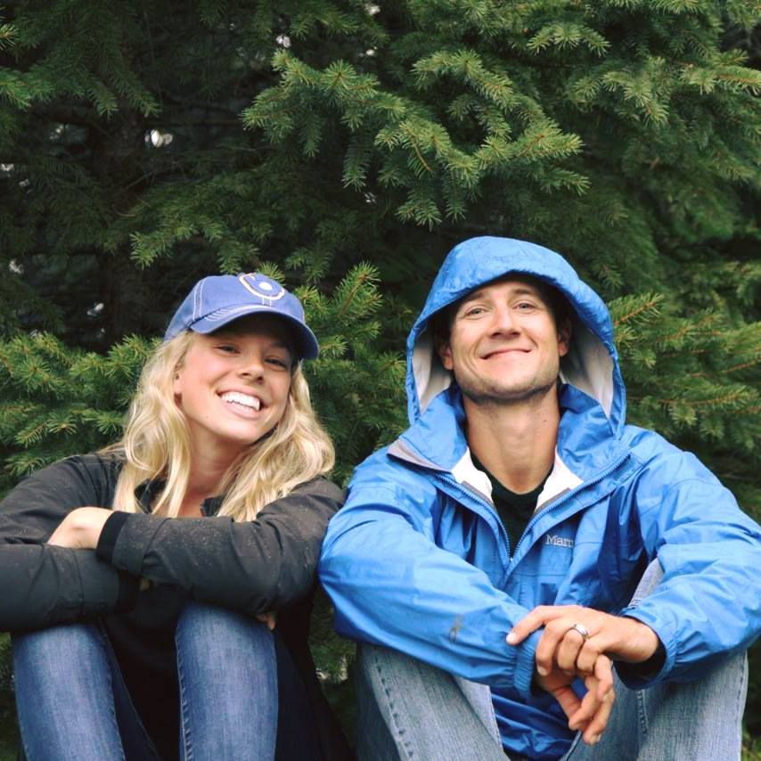 A man and a woman are sitting next to each other in front of trees