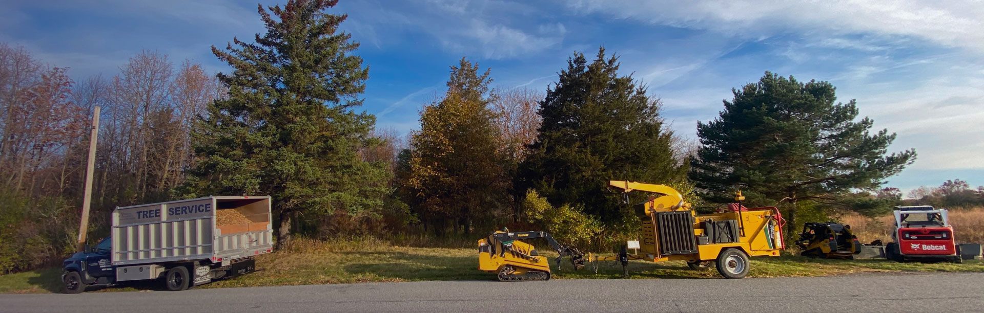 A yellow truck is parked on the side of the road next to trees.
