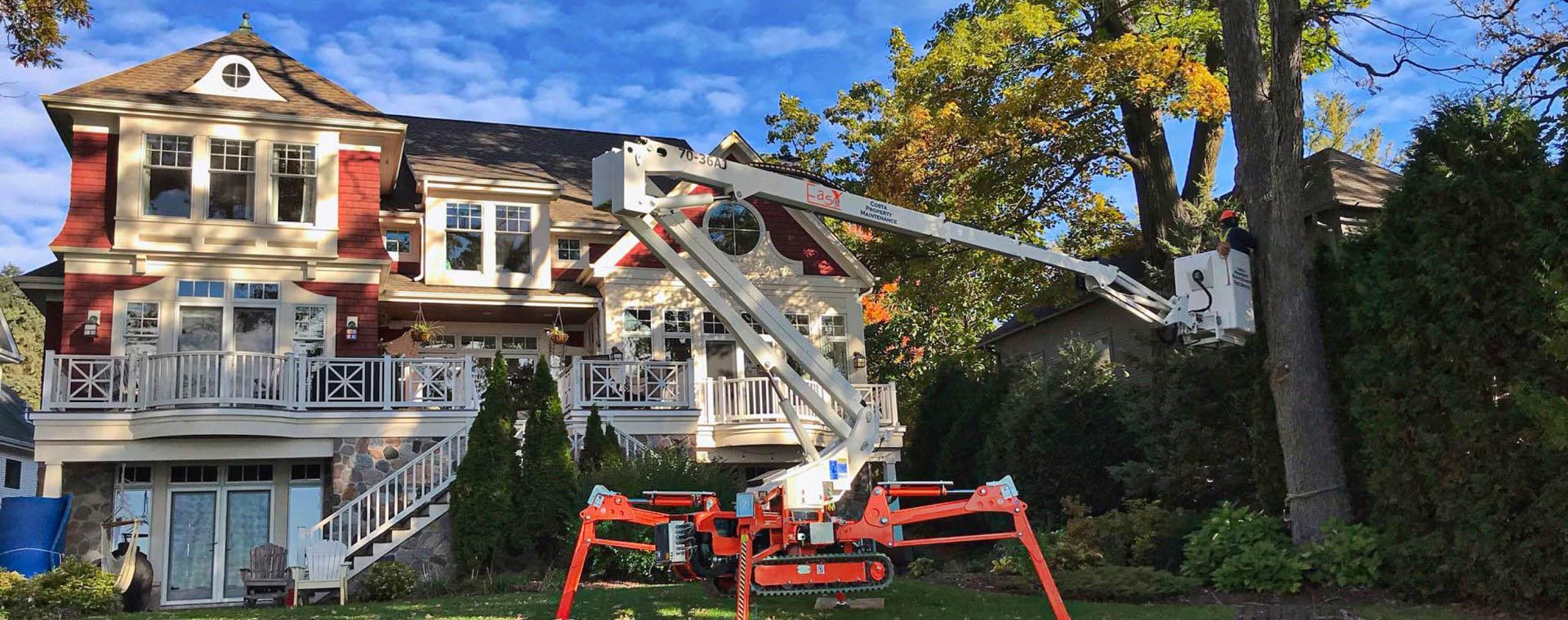 A man is standing on a crane in front of a large house.