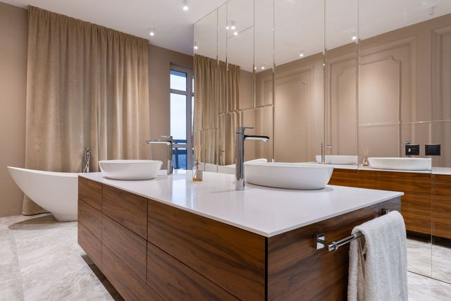 Modern beige bathroom with double vanity, freestanding tub, and large mirrors