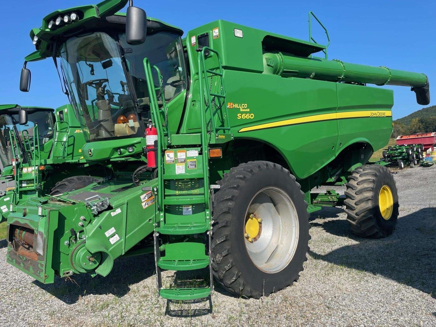 Green combine harvester parked on gravel, front-left view with large tires and extended unloading auger.