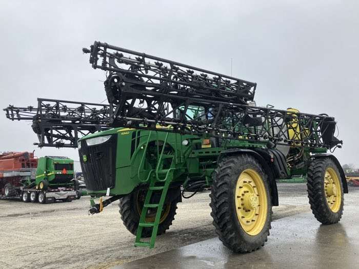 Large green agricultural sprayer with folded booms parked on gravel