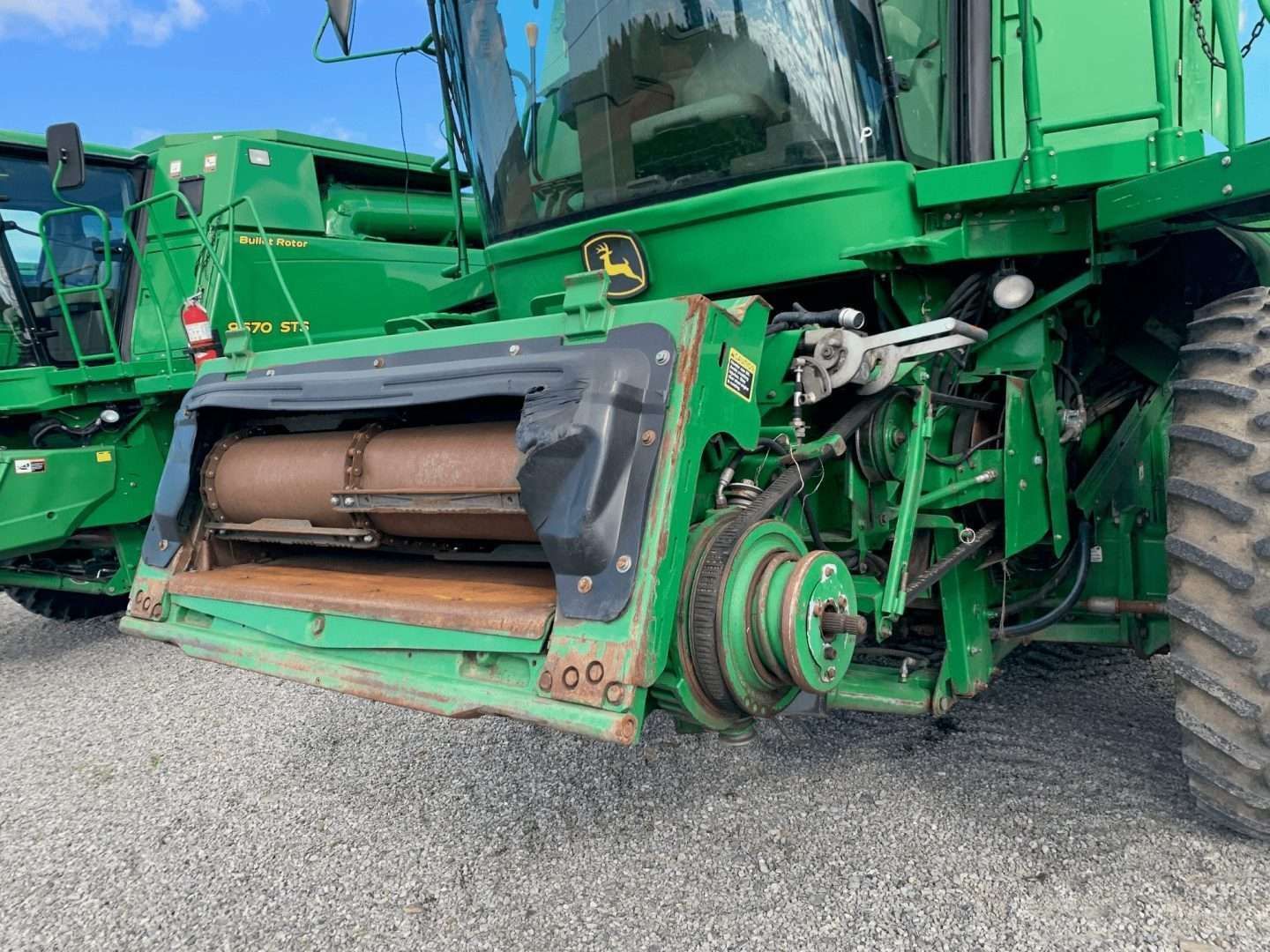 Green combine harvester with a front crop header parked on gravel.
