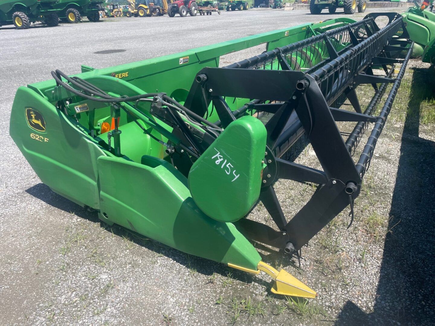 Green combine harvester header with black reel parked on gravel lot in daylight