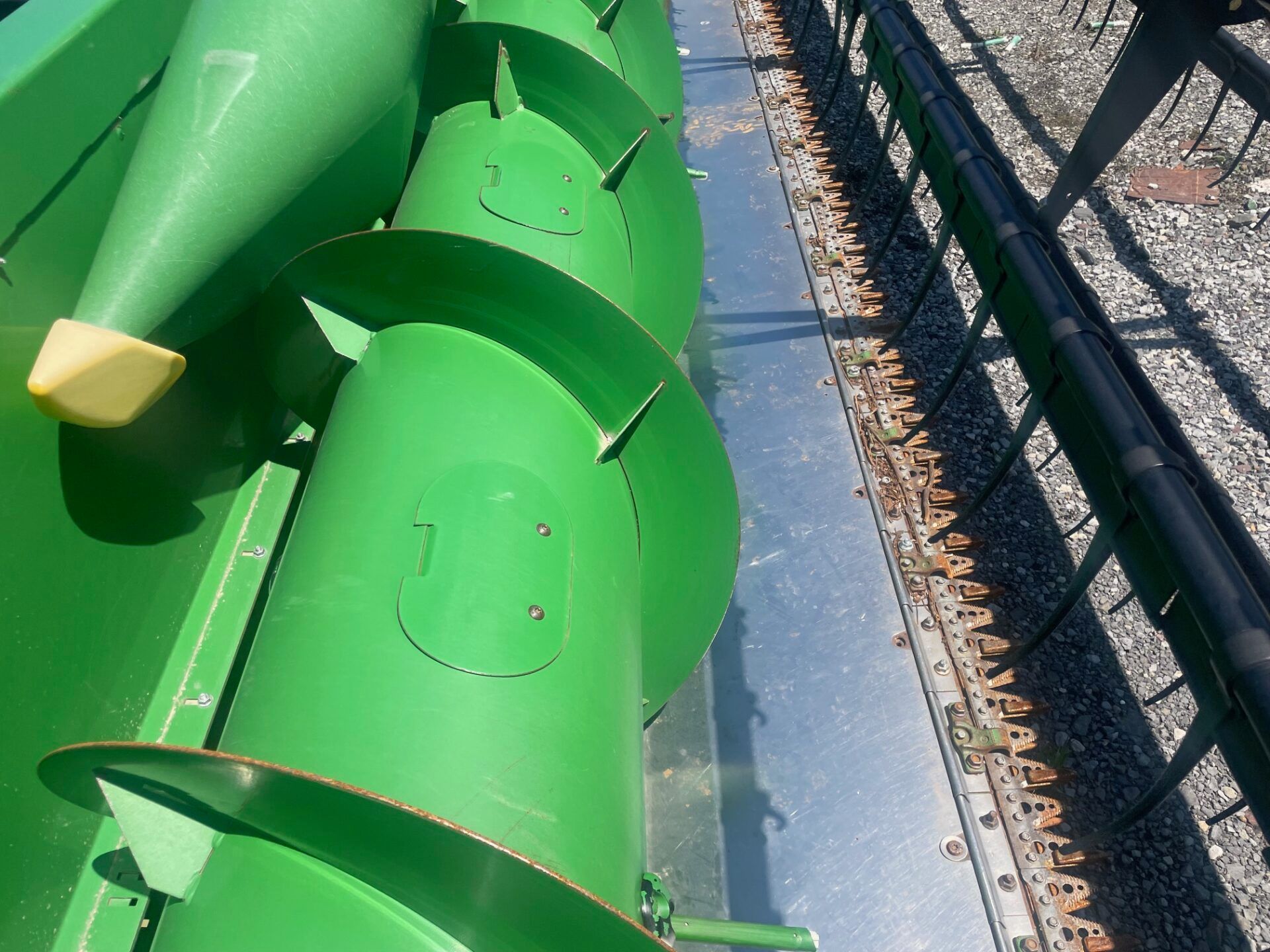 Green playground slide with a yellow handle beside a fence and gravel path