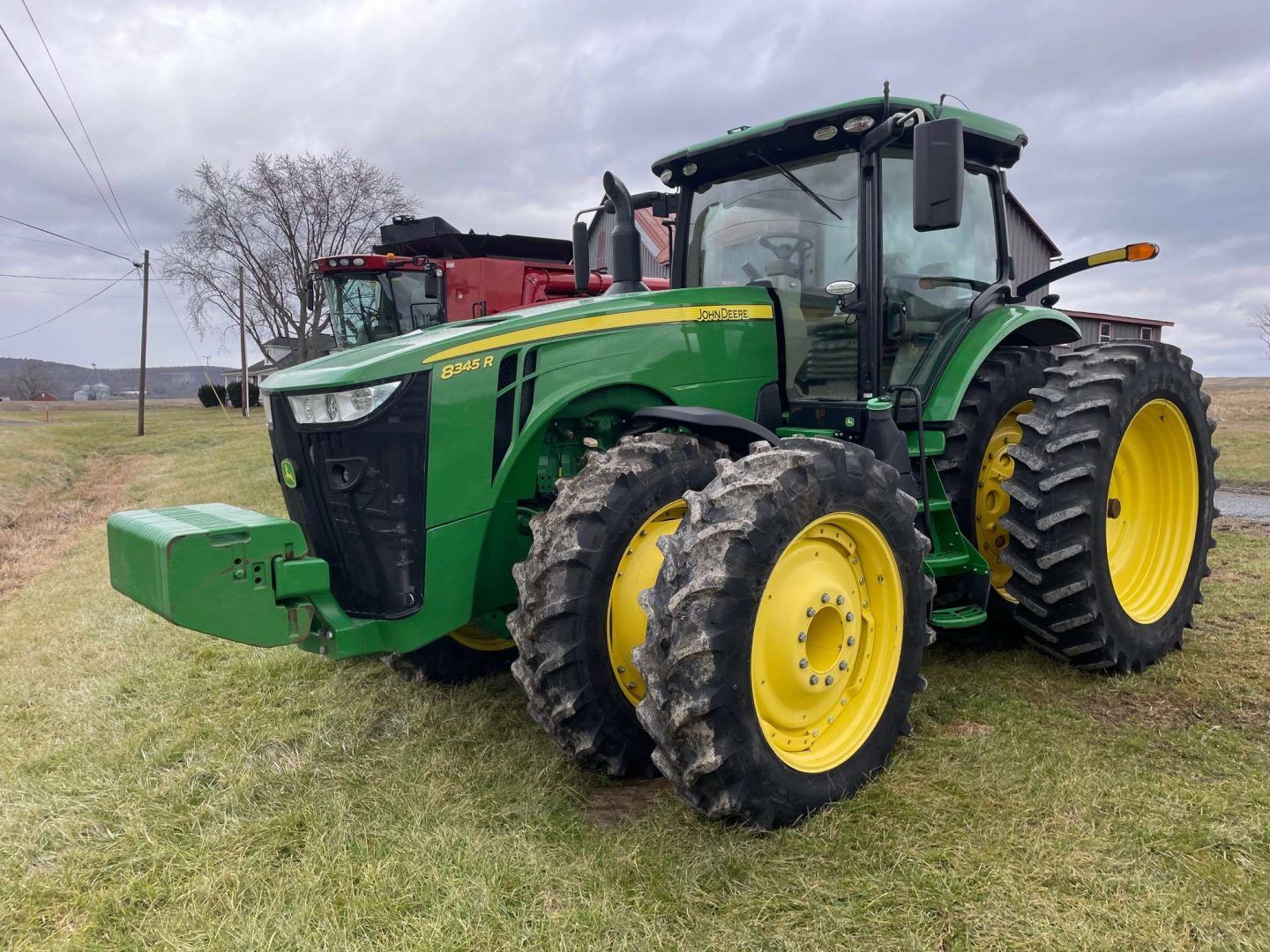 Green John Deere tractor with front weights and yellow wheels parked on a grassy field