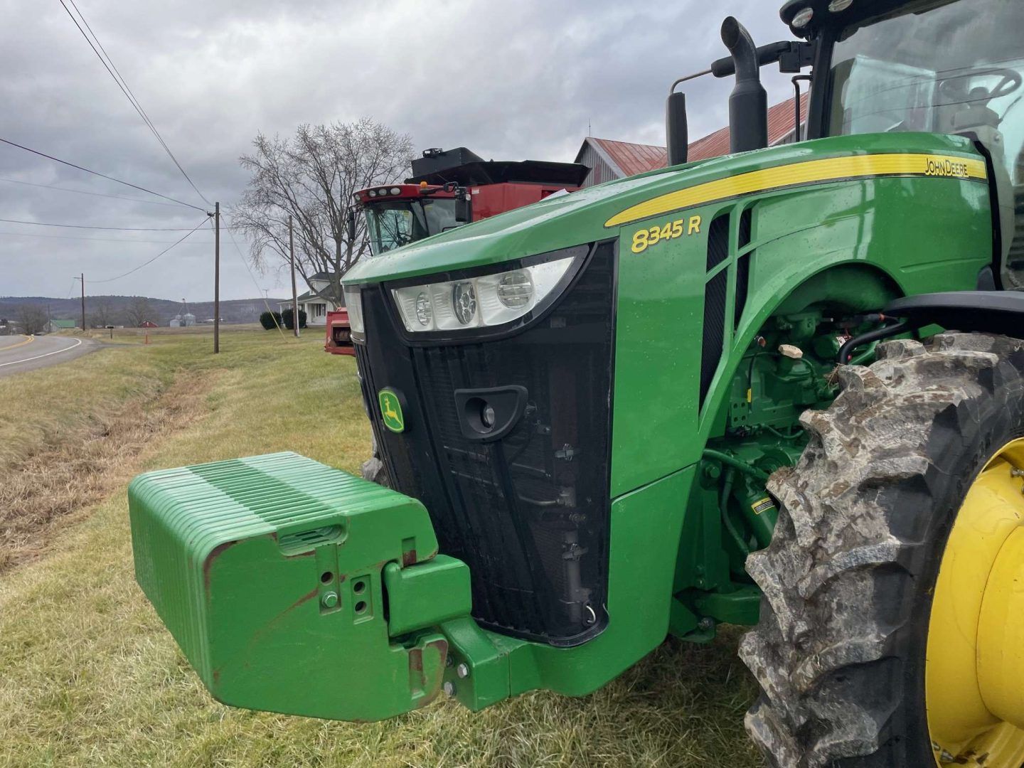 Green John Deere tractor parked beside a rural road on a cloudy day