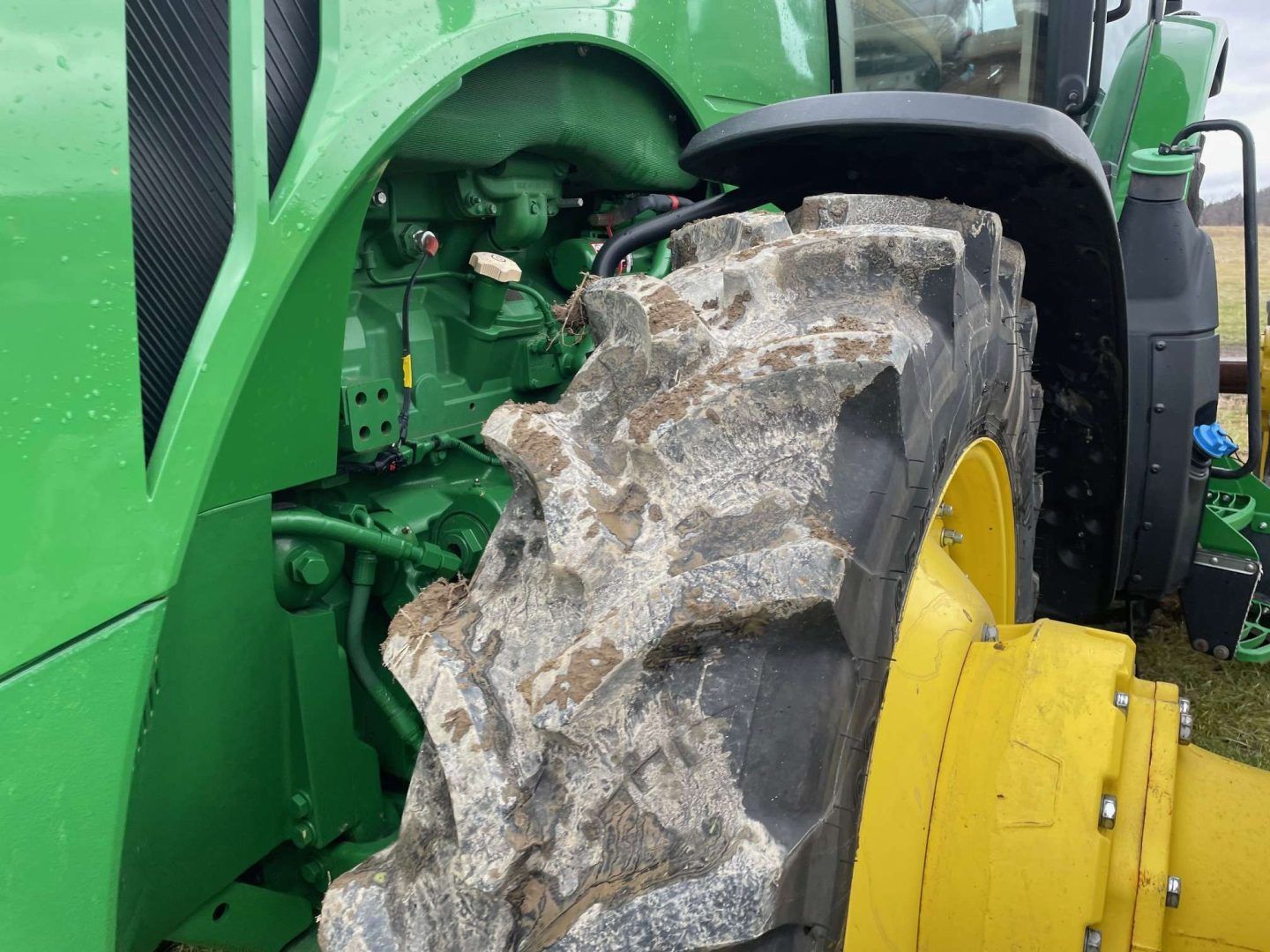 Close-up of a green tractor’s muddy rear tire and yellow wheel hub.