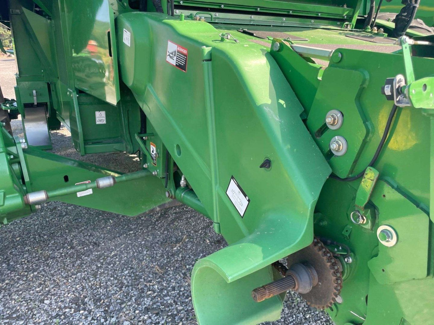 Close-up of a green agricultural machine’s metal hitch and gear assembly on gravel.