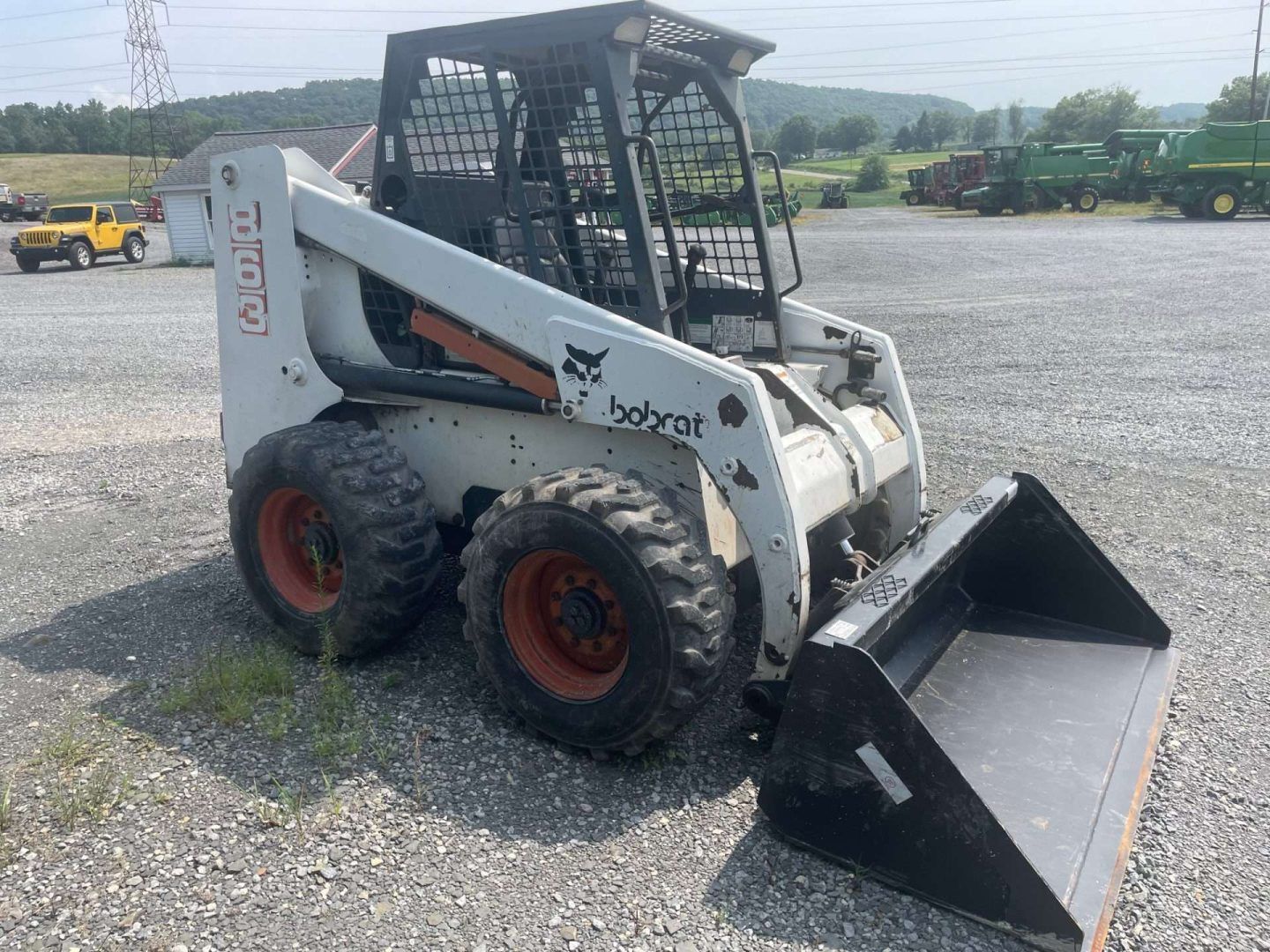 White skid-steer loader with bucket on gravel lot, viewed from the front-left side