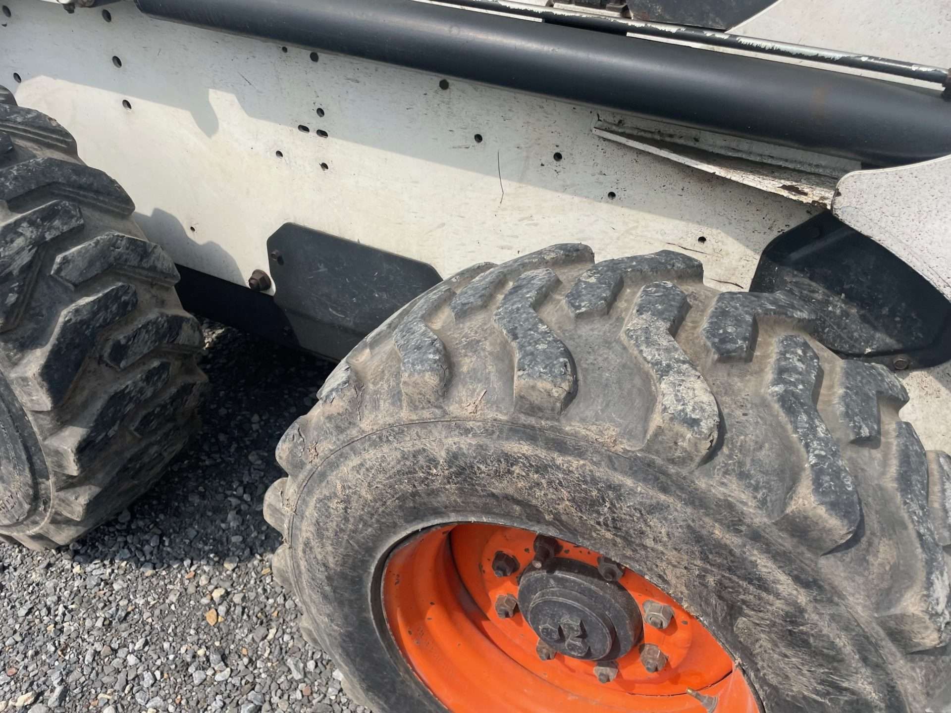 Large off-road tire with orange rim on a gravel surface beside a vehicle