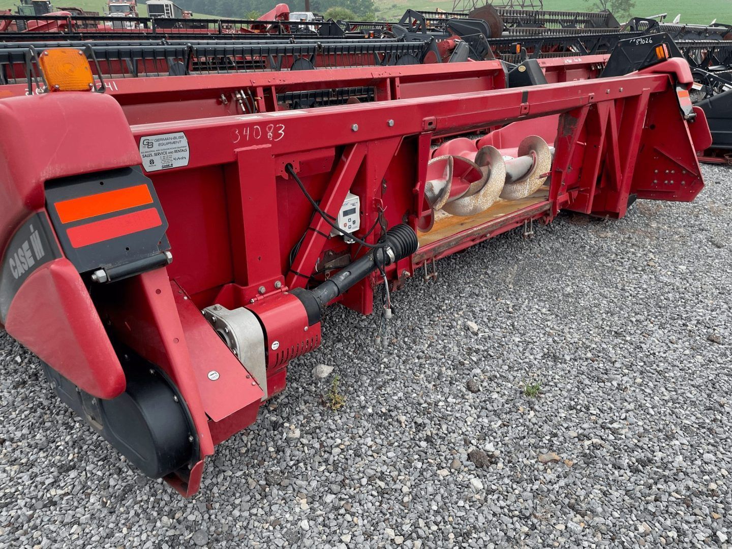 Red farm implement with metal blades and black wheel, parked on gravel lot