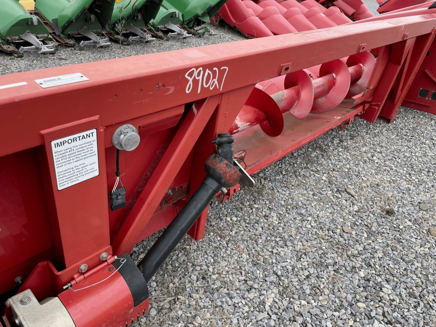 Red agricultural machine with red auger and hydraulic arm on gravel lot