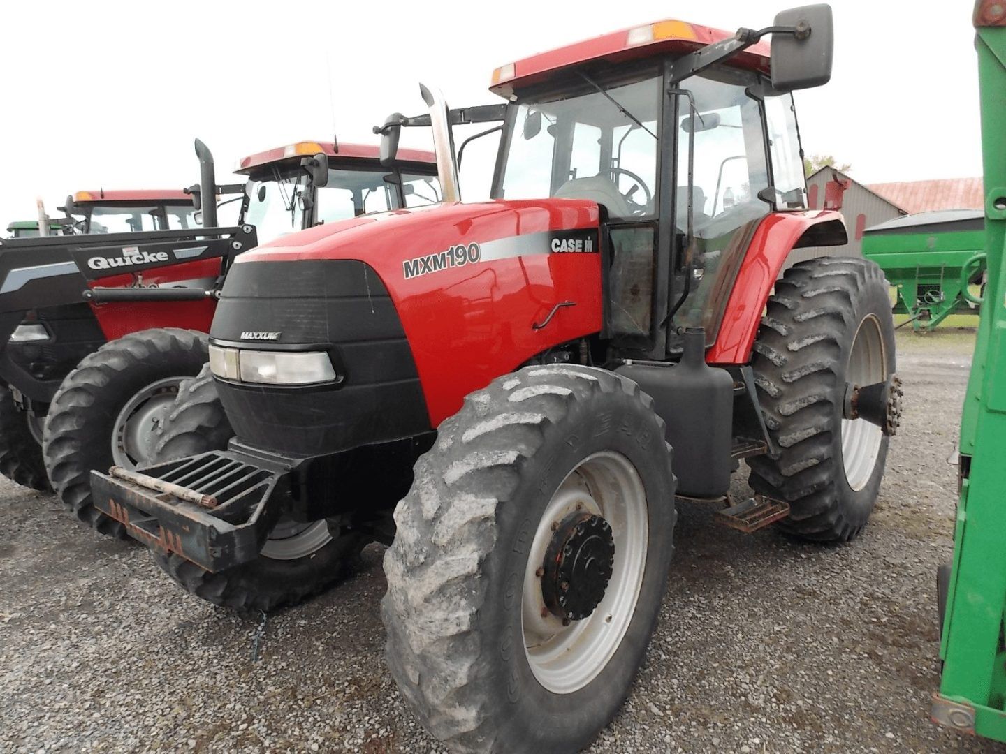 Red farm tractor parked on gravel, with large tires and a cab, beside other tractors.