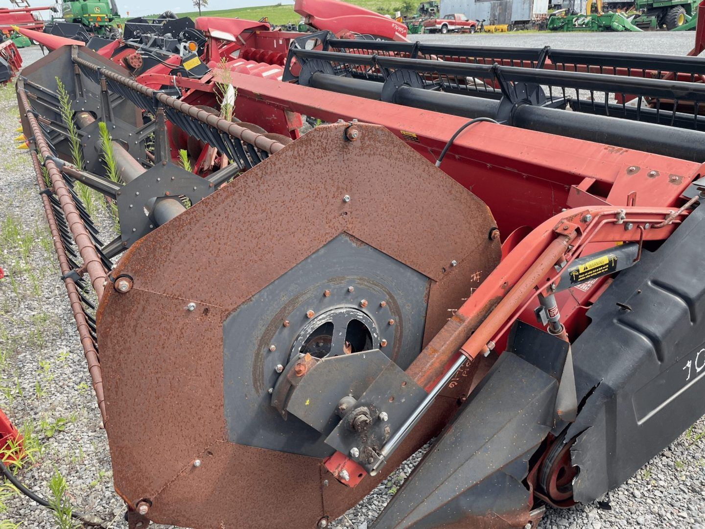 Rusty red farm machinery with a large round metal reel and black cutting bar outdoors.