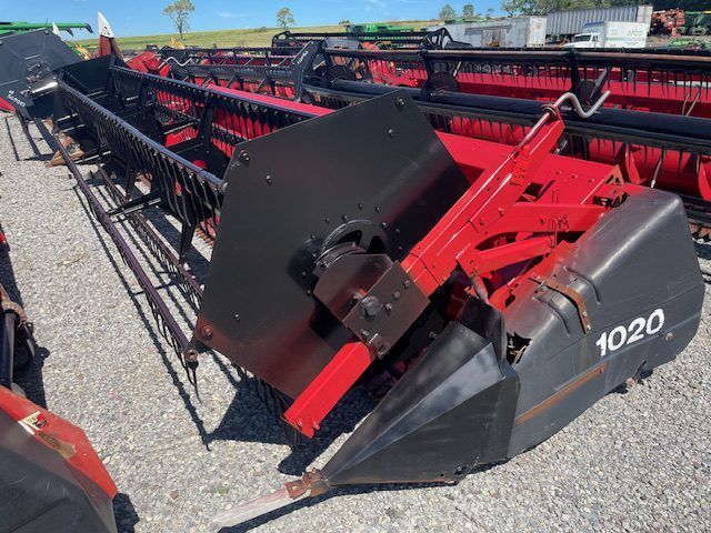 Red-and-black farm combine header on gravel lot, marked “1020”