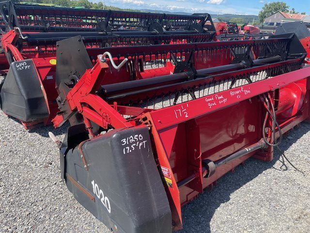 Red agricultural harvesting machines with black reels parked outdoors on gravel