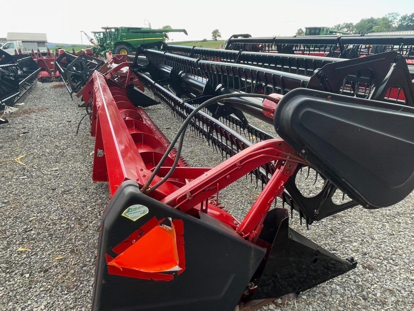 Red agricultural header with black reel and orange reflective marker on a farm equipment lot.