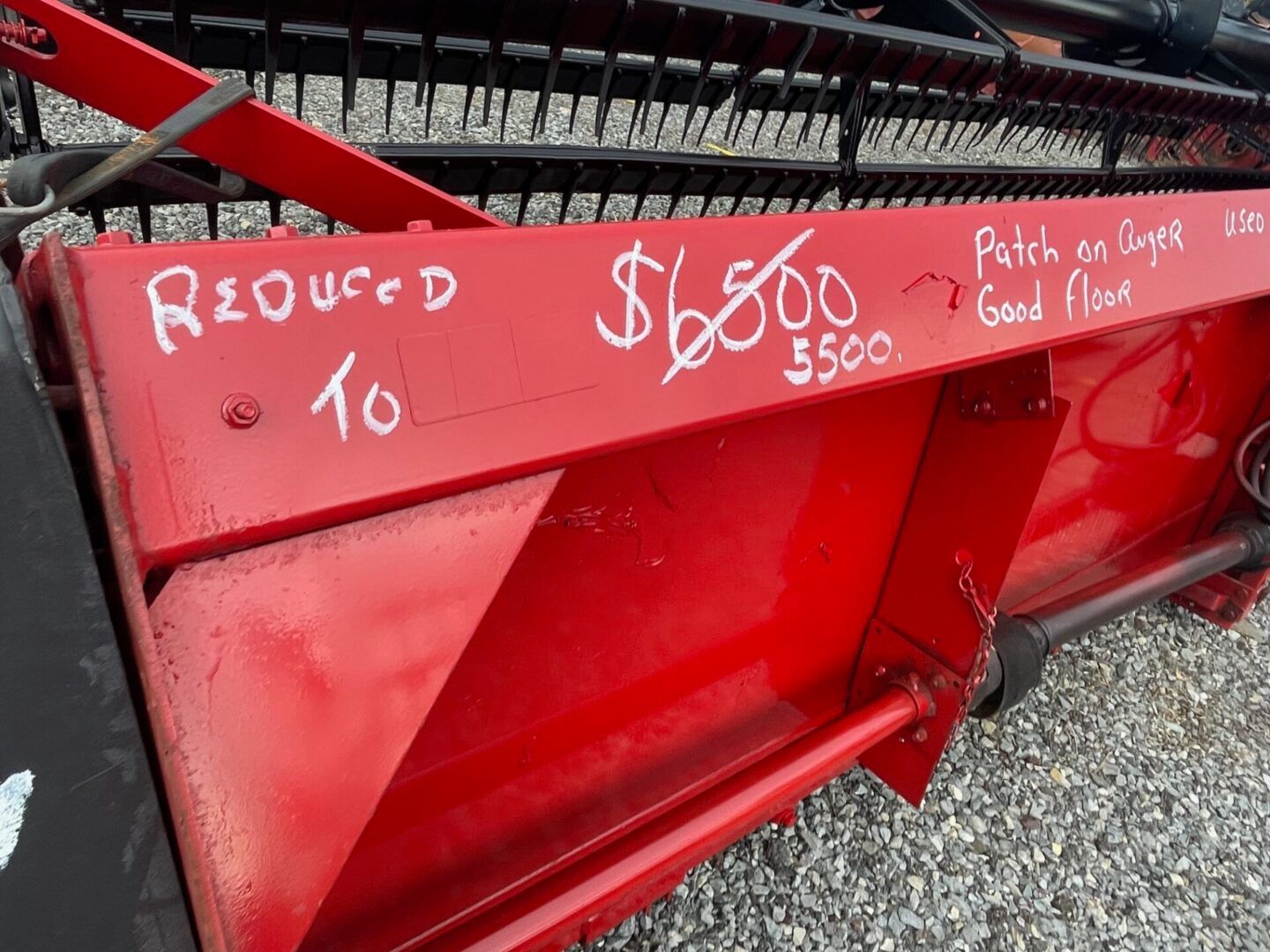Red metal machine panel marked “Reduced to $800” on gravel, with handwritten notes and signs.