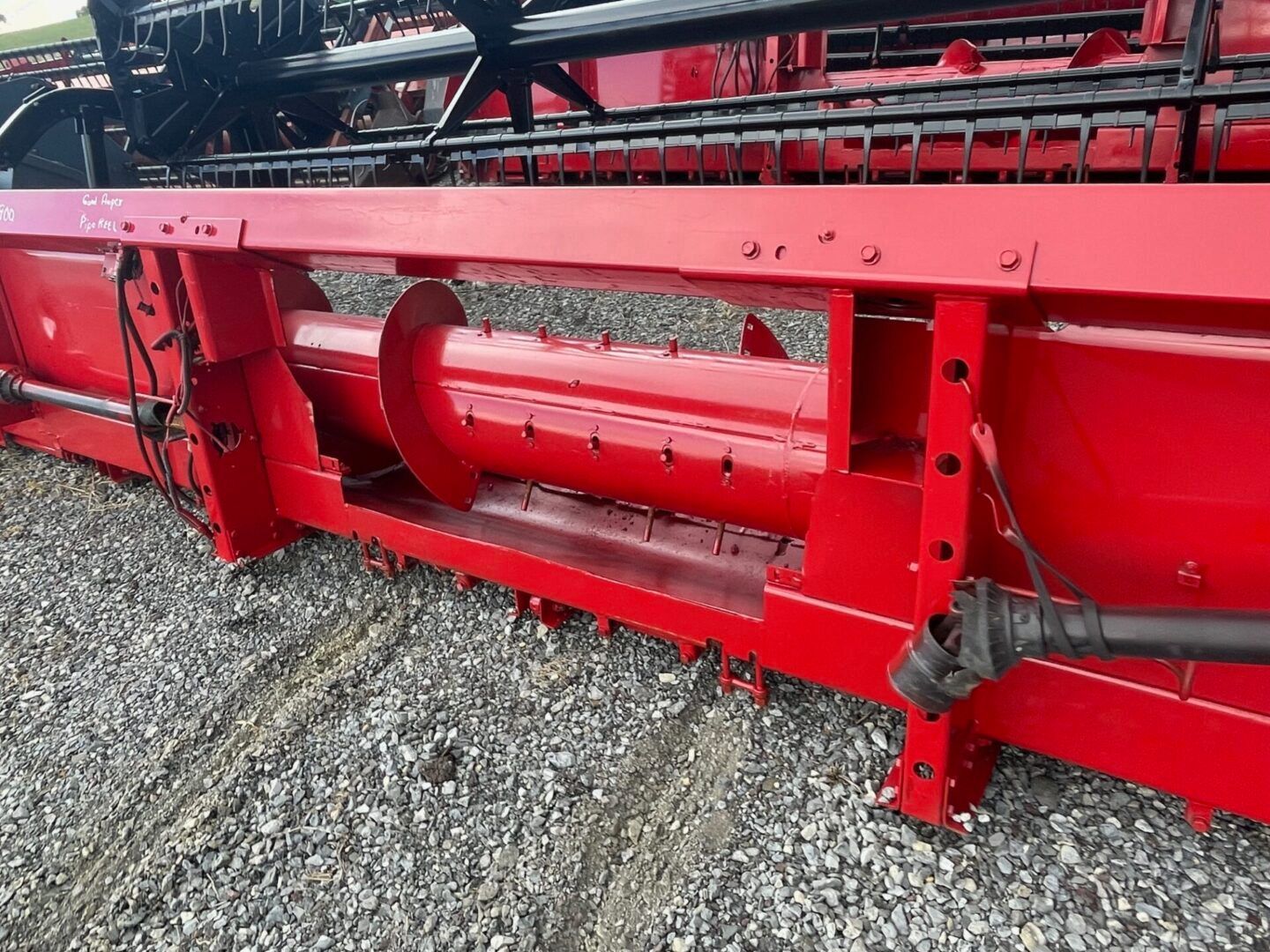 Close-up of a red farm combine header on gravel, showing the cutting reel and metal frame