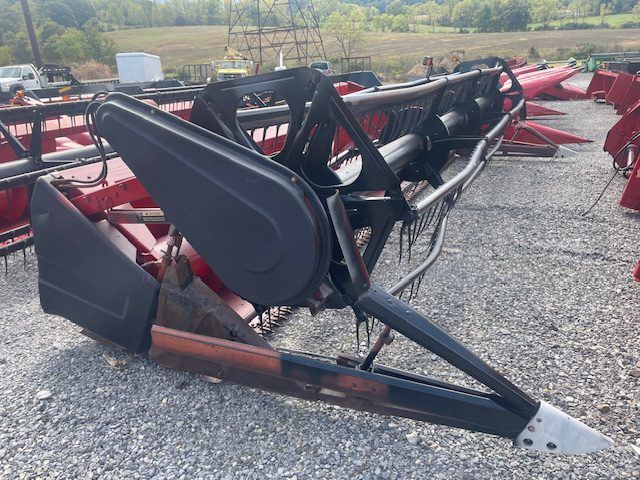 Black agricultural implement on red trailer in gravel lot with fields in the background